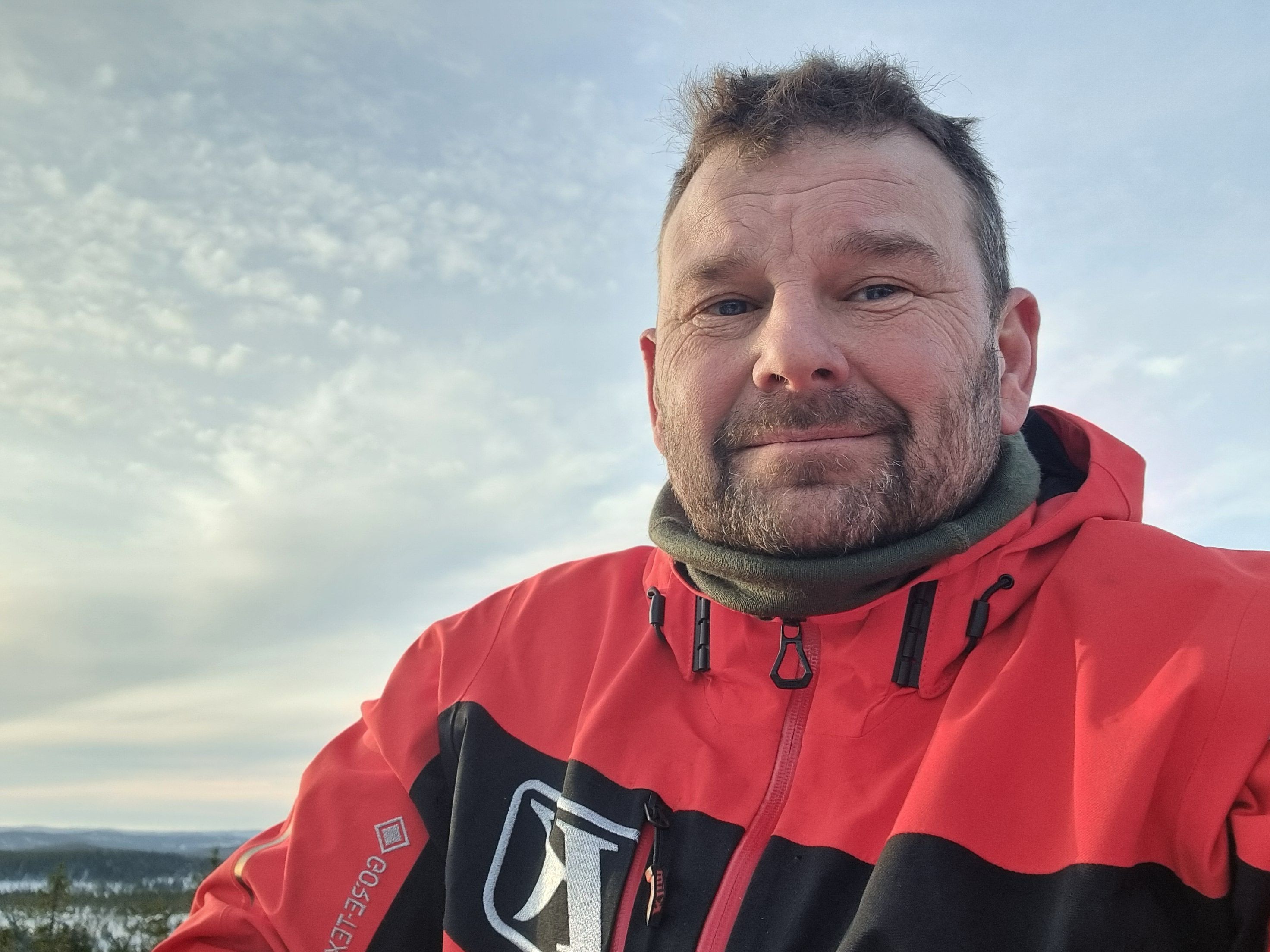 Person i röd vinterjacka utomhus med snötäckt landskap i bakgrunden