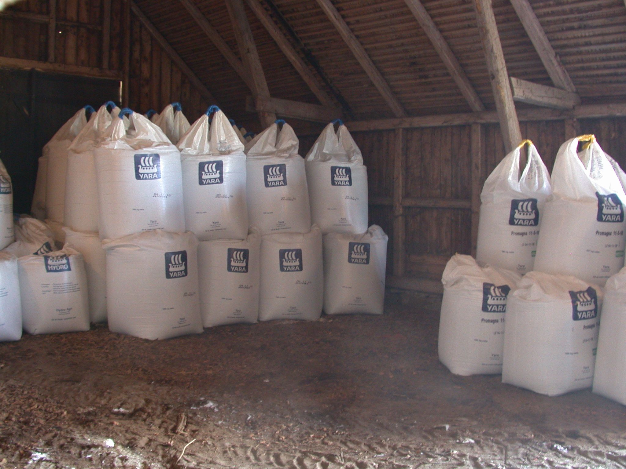 Stora vita gödselsäckar staplade inne i en lantlig trälada