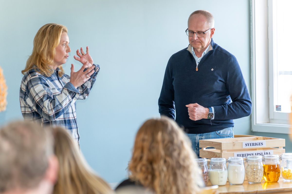 Två personer håller en presentation framför publik med burkar på bordet