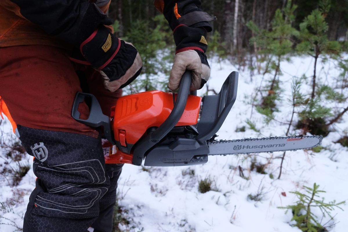Person i skogsutrustning håller i en motorsåg från Husqvarna i snötäckt skog