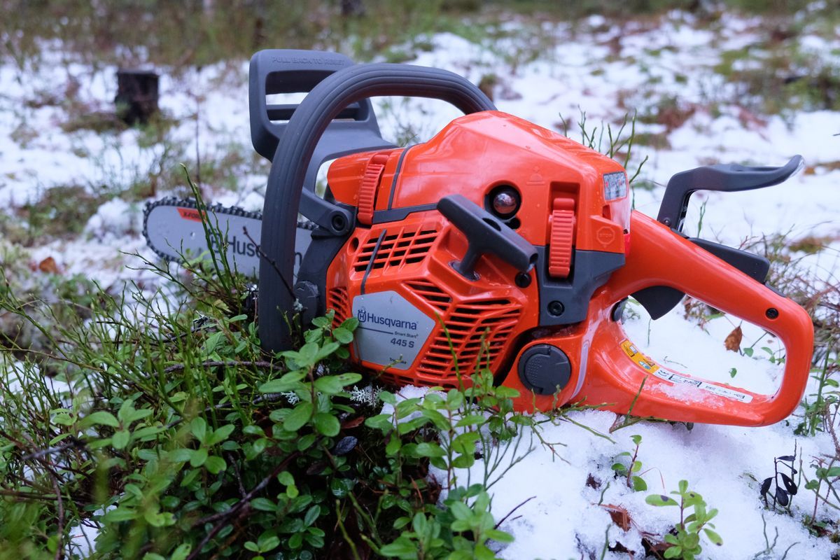 Orange Husqvarna motorsåg liggande på snötäckt mark bland gröna växter