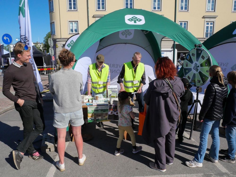 Människor i kö vid ett informationsstånd på en marknad.