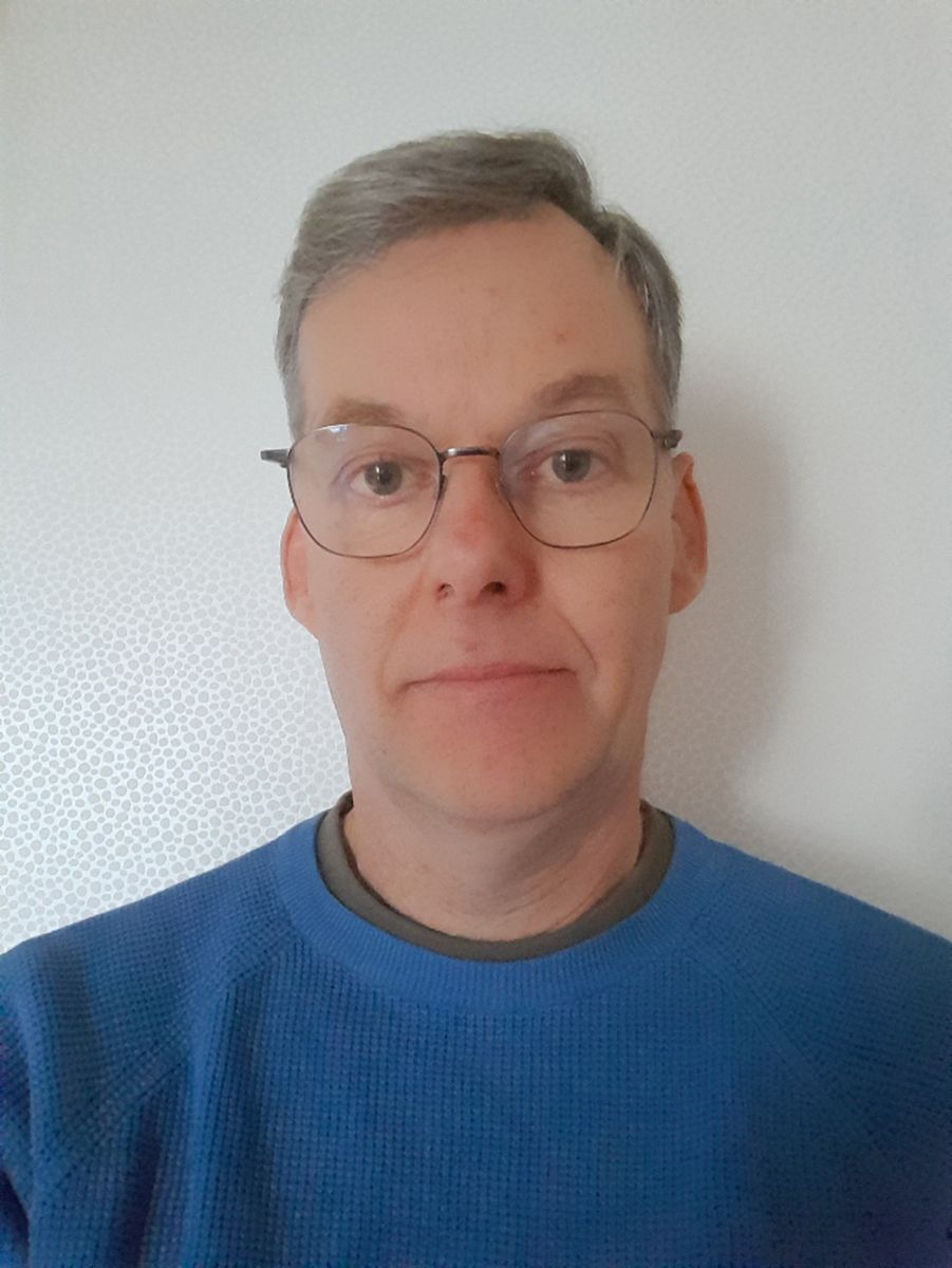 Porträtt av person med glasögon och blå tröja mot ljus bakgrund