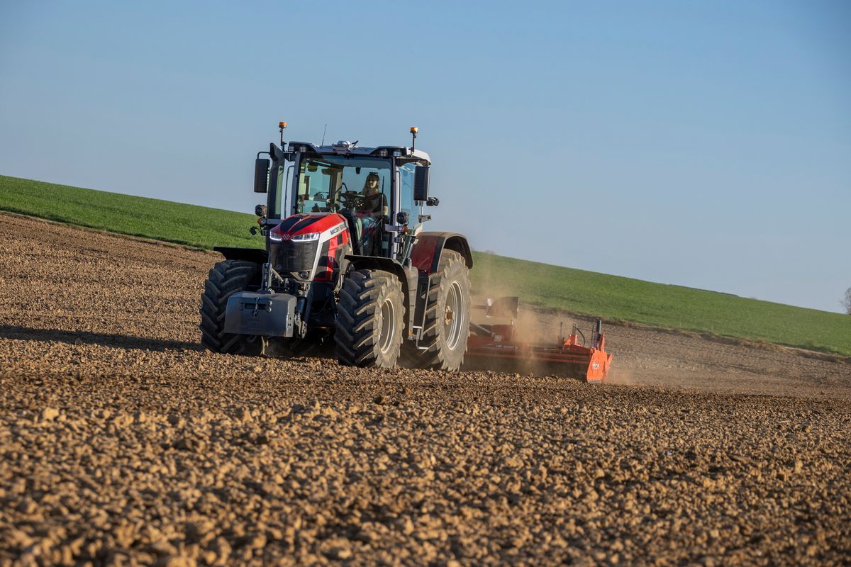 Traktor som bearbetar en åker och sprider damm på en solig dag