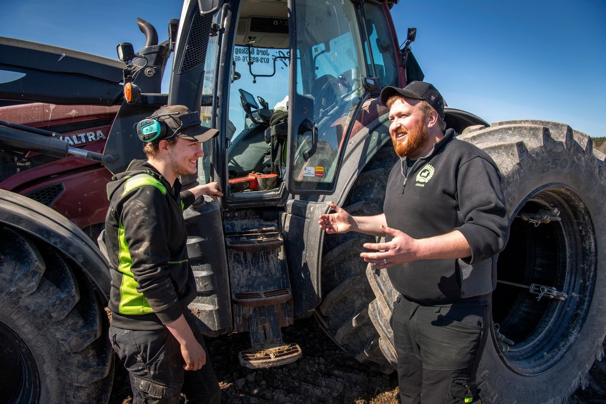 Två lantbrukare samtalar vid en lerig traktor på åkern en solig dag