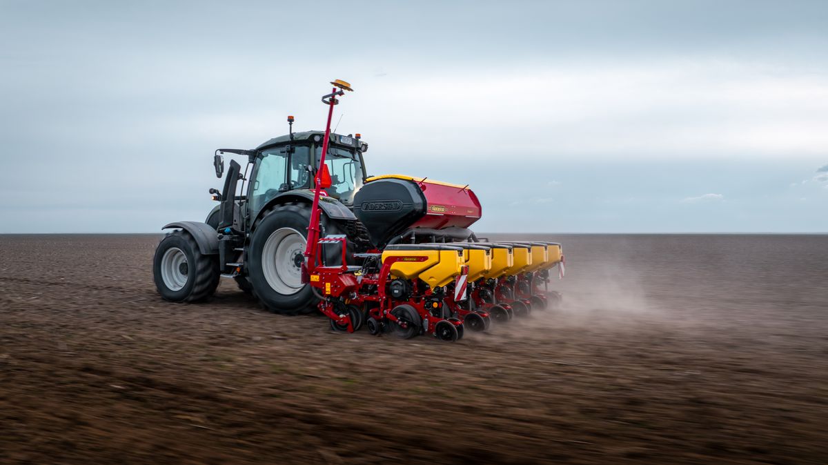 Traktor med såmaskin arbetar på en stor åker under mulen himmel