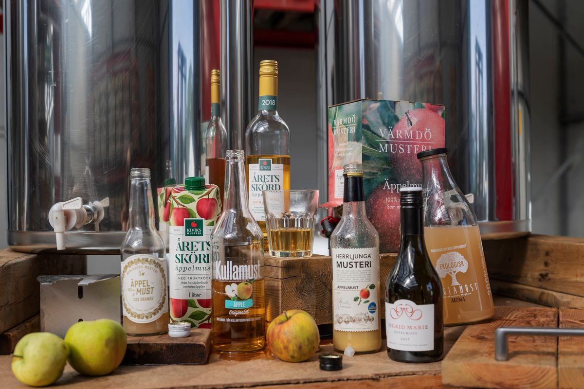 Olika sorters äppelmust och cider framför stora ståltankar i bryggeri
