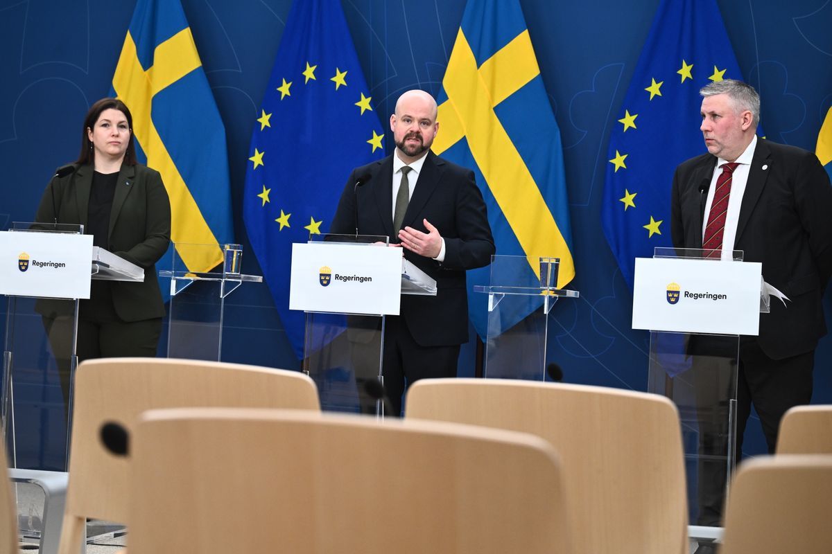 Presskonferens med tre talare framför svenska och EU-flaggor i en sal