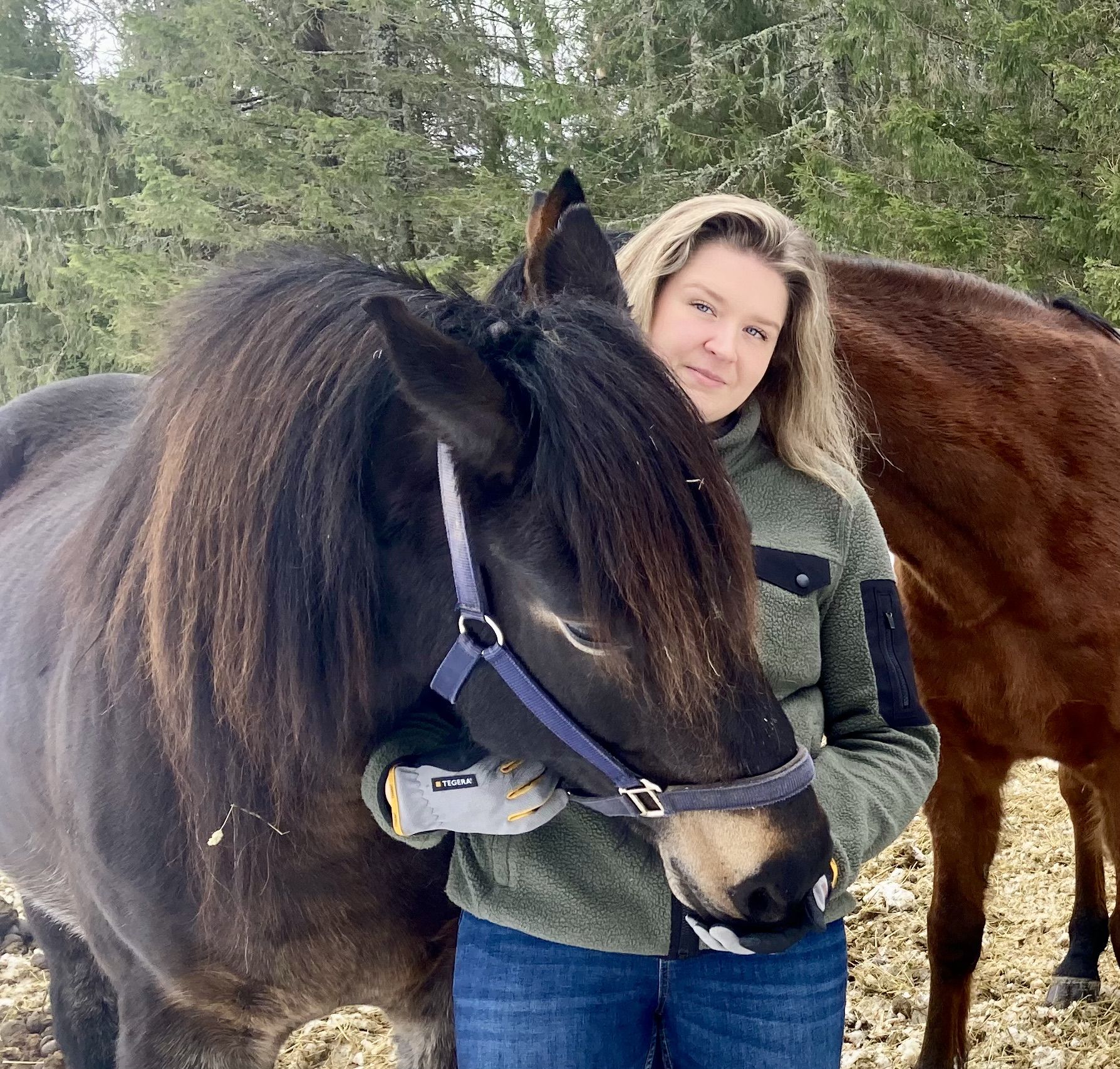 Sofia Lundgren står utomhus och kramar en mörkbrun häst framför skog.
