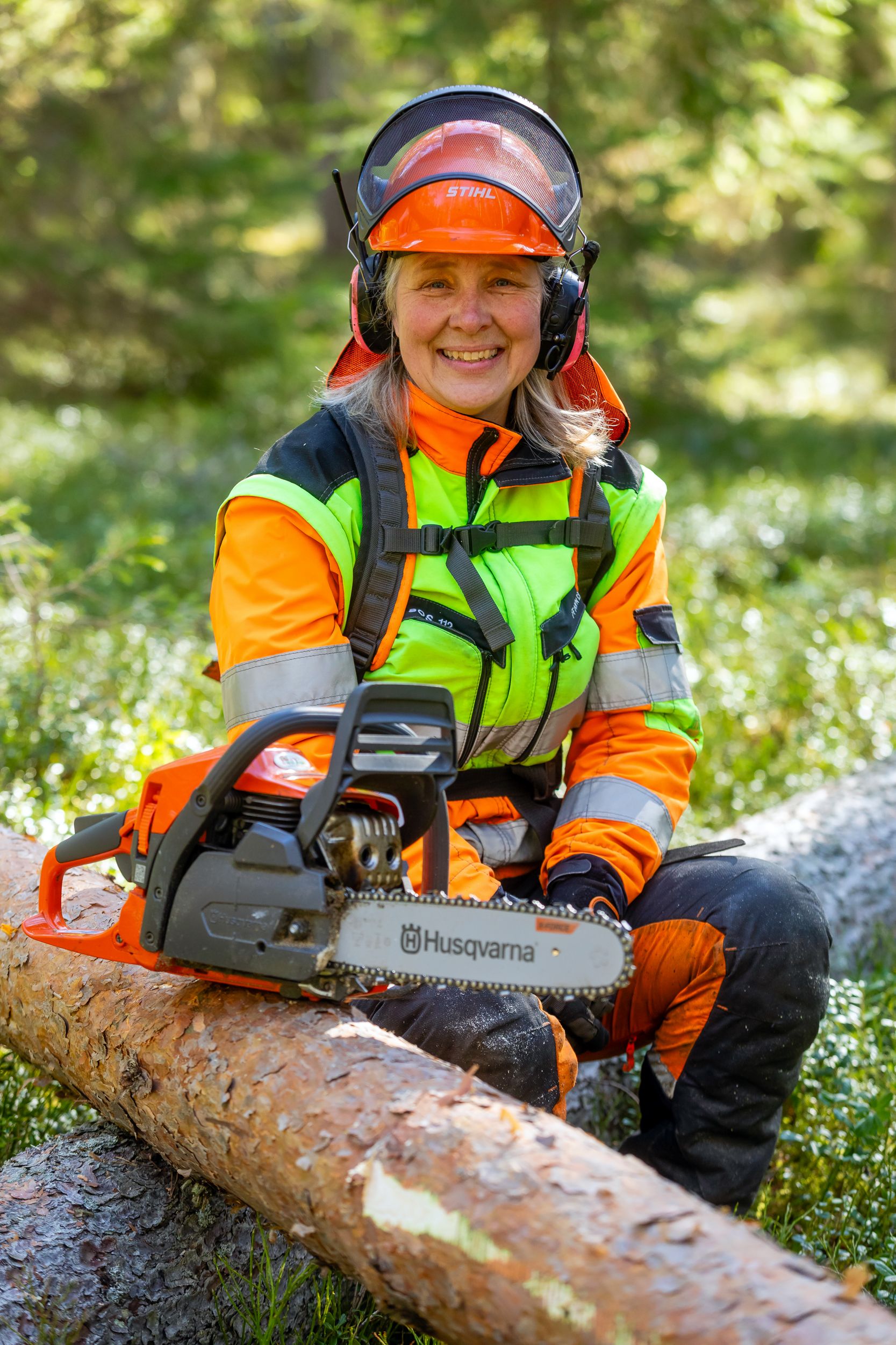 Skogsarbetare i orange skyddskläder sågar stock med motorsåg i skogen